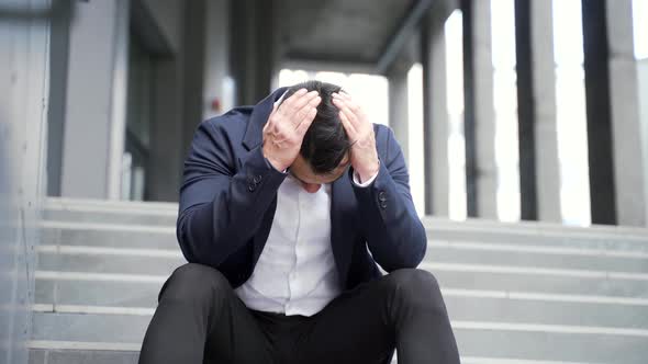 young asian depressed man sitting on the stairs outdoors street near office business 