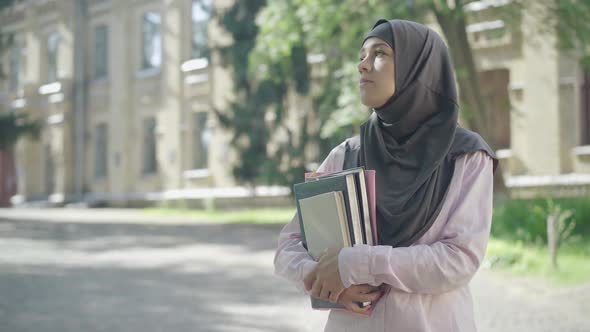 Sad Young Muslim Woman Holding Books in Hands and Waiting Outdoors. Portrait of Beautiful Upset