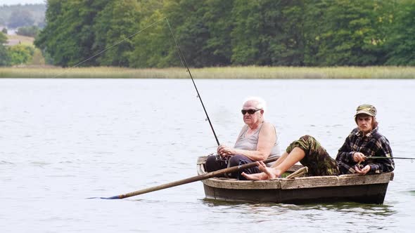 Old angler with a grandson sitting in the boat on the lake with a rod while fishing. Outside.