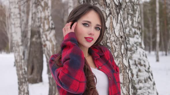 Young Woman with Wavy Hair Standing and Touching Face in Winter Forest