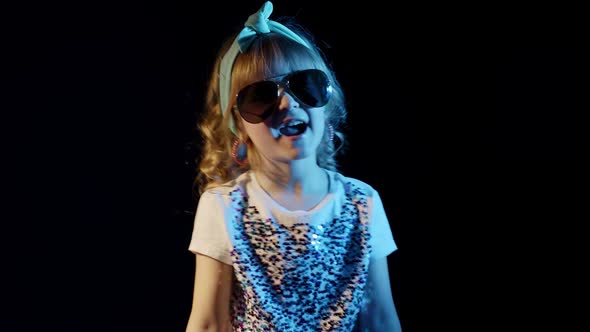 Playful Blond Girl in Blue Neon Lights Singing on Black Background Making Faces Fooling Around