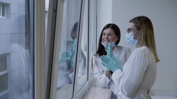 Medical Assistants Looking at the Window Rejoicing and Clapping Hands in Clinic