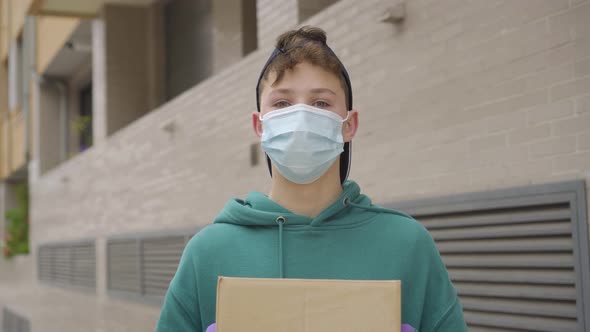 A delivery man wearing a medical mask and protective gloves  holds a cardboard box