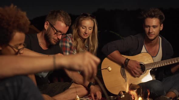 Young Caucasian Male Playing Guitar While Friends Sitting Around Listenning Talking Smiling Eating