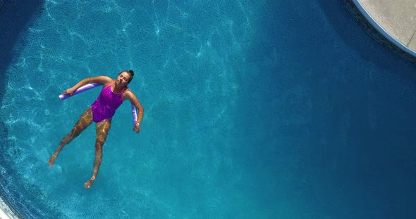 Young girl relaxing on a noodle in a large backyard swimming pool.