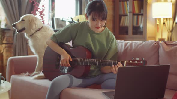 Asian Woman Petting Dog and Learning Guitar Online at Home