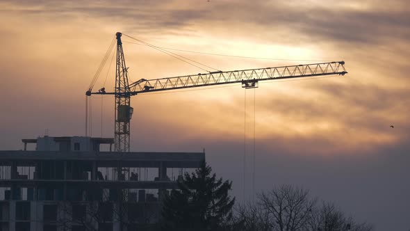 Dark Silhouette of Tower Crane at High Residential Apartment Buildings Construction Site at Sunset