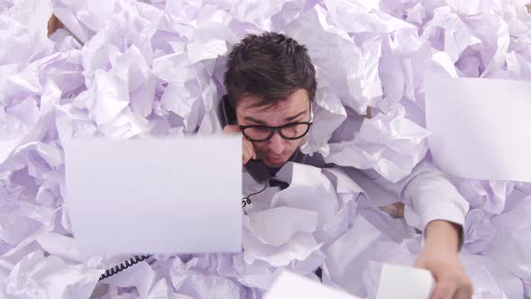 Confused Man Office Worker Is Talking on the Phone in a Large Heaps of Paper