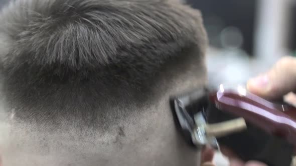 Barber Uses a Clipper To Cut the Client's Hair in a Chair. Close-up Clipper Shaves Off Hair