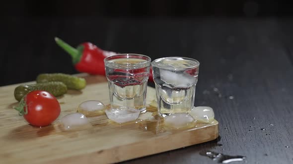Vodka in Shot Glasses on Rustic Wood Board. Adding Ice Cubes.
