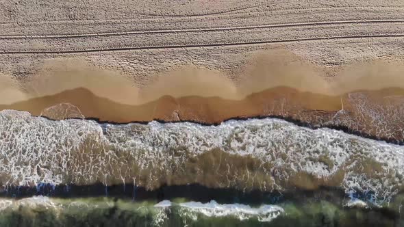 Aerial footage overlooking a beautiful clear water ocean showing tyre tracks on the beach