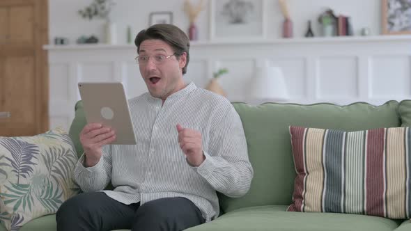 Man Celebrating Success on Tablet on Sofa