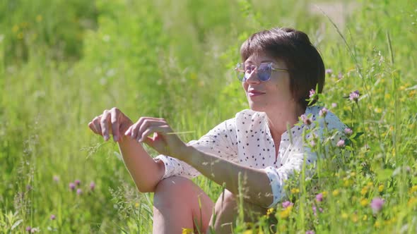 Woman in Colorful Sunglasses Enjoys Sunlight and Flower Fragrance on Grass Field