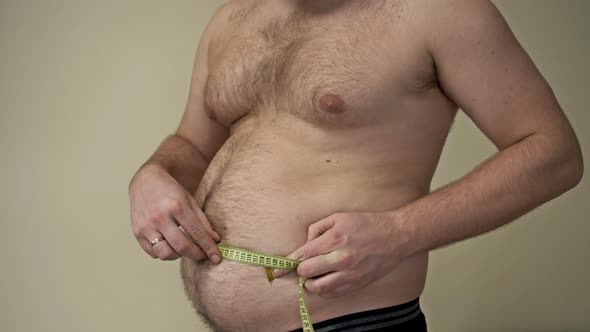 Fat Man Measures His Waist Circumference with a Tape Measure and Shows the Folds of Excess Fat on