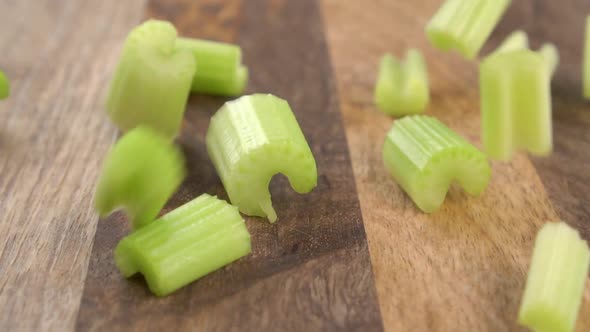 Fresh chopped green celery stem. Falling slices on a rustic wooden surface. Slow motion