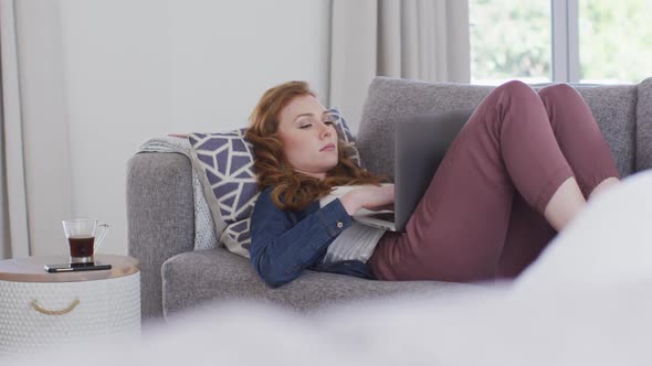 Woman using laptop while lying on the couch at home