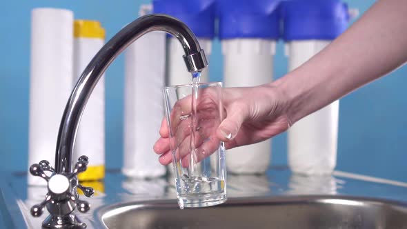 Hand Pours Clean Drinking Water From Under the Filter on a Blue Background