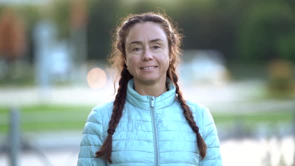 Charming Smiling Middle-aged Woman Is Looking at Camera, Standing Outdoors in City