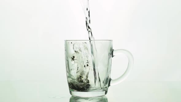 Black Tea Particles Pouring Into Glass Transparent Mug and Adding Boiling Water To Brew Tea Isolated