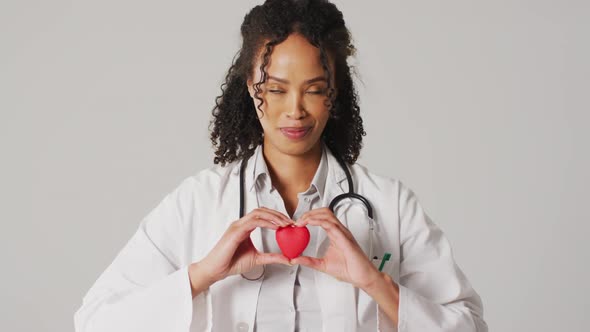 Video of portrait of smiling biracial female doctor holding heart on white background