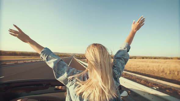 Woman with Hands Up Outstretched Stands in Front Seat of Cabriolet View From Back