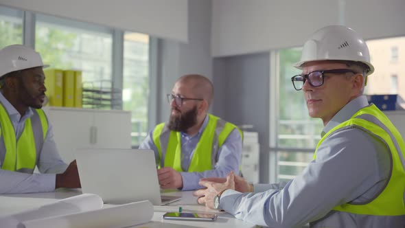 Mature Engineer Smiling at Camera Sitting at Desk with Colleagues