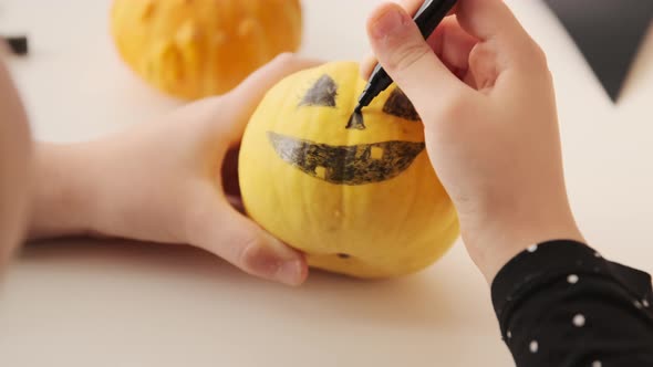 Little kid preparing for holiday Halloween. Hands of children drawing scary face on pumpkin