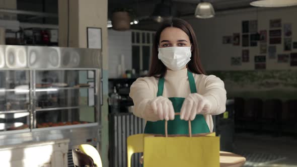 Waitress in Mask and Gloves Holding Bag with Takeaway Meal