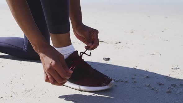 African American woman tying her shoe on the beach and blue sky background