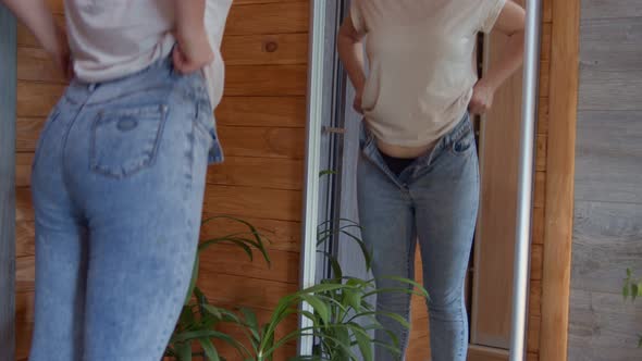 Adult Woman Pulling Up Tight Jeans After Gaining Weight While Standing in Front of Mirror