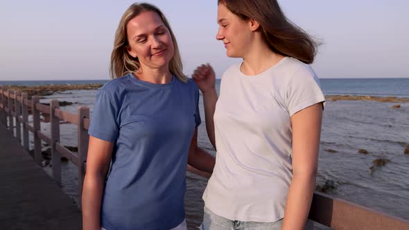 Mother and daughter standing on sidewalk by the sea at sunset and talking