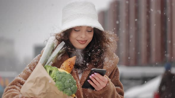 A Woman is Walking Through the Parking Lot Near a Supermarket and Texting on a Smartphone