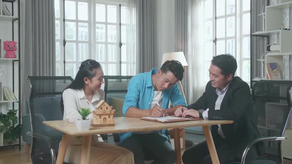 Asian Man Sitting With A Woman And A Real Estate Agent Signing On House Purchase Contract Paper