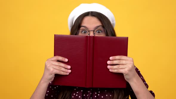 Happy Surprised Nerd Teen Girl in Glasses Hiding Behind Reading Book Making Smart Face Reader