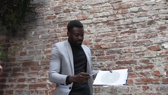 Handsome Afro American Businessman Uses Financial Document with Graphs to Familiarization