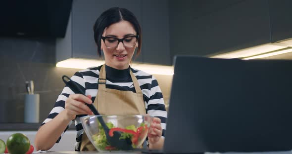 Woman in Glasses Watching Movie on Laptop and Mixing Vegetable Salad in Bowl Using Spoon