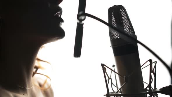 Beautiful woman singing into a microphone in a recording studio. Black and white. Female silhouette