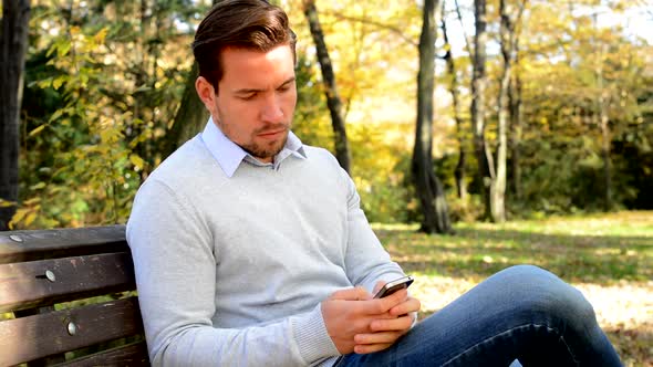 Young Man Sits on Bench in the Park, Thinks About Something and Works  on the Phone