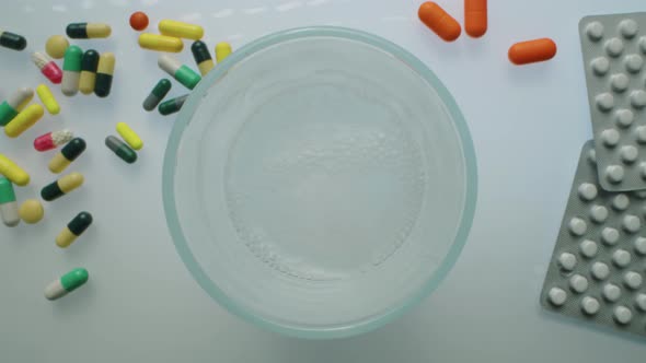 Dropping Effervescent Tablet into Glass on Water on Desk with Medicines