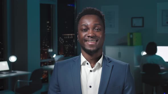 Medium Shot of Happy AfricanAmerican Businessman Smiling at Camera Standing in Dark Office