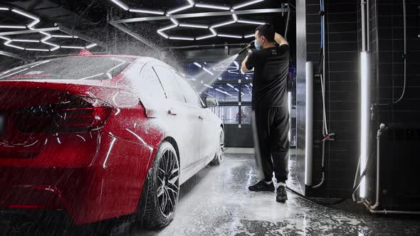 A Man Covers the Car with a Thick Layer of Foam Using a Sprayer