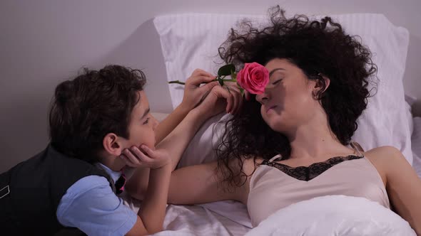 Close Up Child Awakening Mom in Bed with Rose