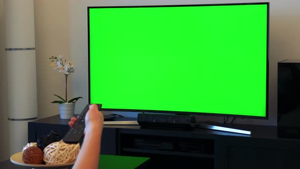 A Woman Switches Channels on a TV with a Green Screen