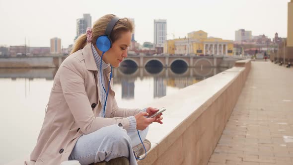 35 Years Old Woman in Headphones and Listens to Relaxing Music and Singing Outdoor