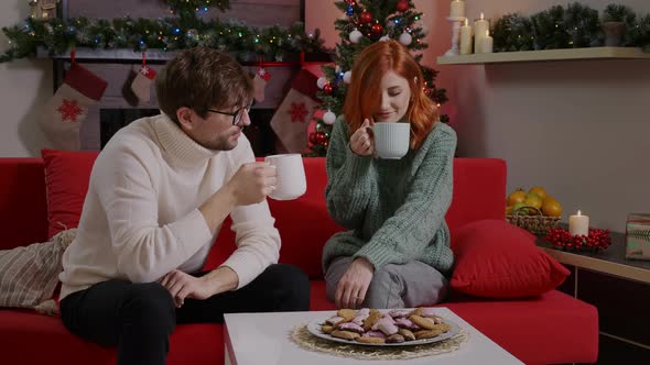 A couple drinking tea and talking over a Christmas decorated livingroom