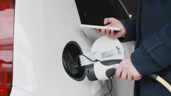 Close Up Woman Hand Plugging Power Cord to an Electric Car and Paying Using Her Smartphone