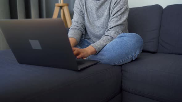 Woman Sitting on a Cozy Sofa and Working on a Laptop. Concept of Remote Work.