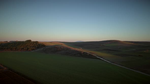 Aerial view of beautiful hills with lots of grass and trees at sunset.