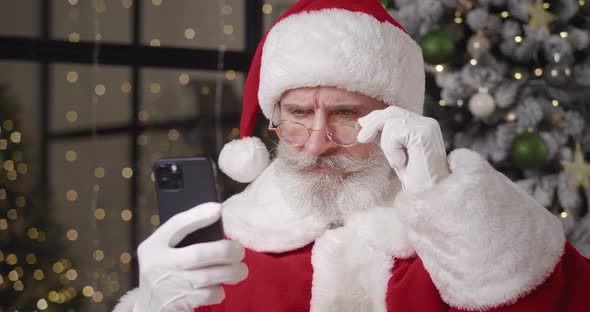 Closeup Portrait of a Brooding Santa Reads the Message on His Smartphone Through His Lowered