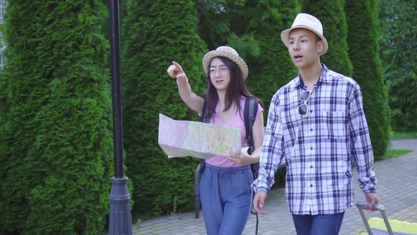 Positive Young Man and Woman Asian Travelers with Suitcase and Card in Hand in the Park